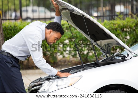 Closeup portrait, young man having trouble with his broken auto, opening hood trying to fix engine, isolated green trees outside background. Car won\'t start, dead battery