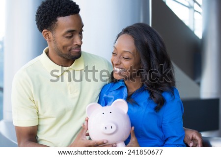 Closeup portrait, happy handsome couple or two business people holding pink piggy bank looking at each other, laughing.  Smart financial decisions