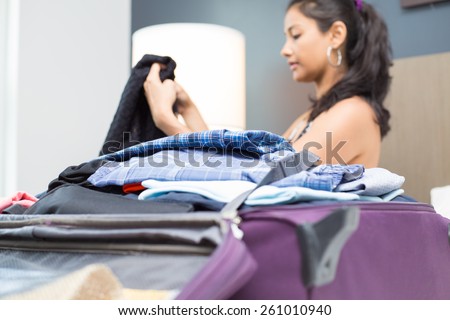 Closeup portrait, young woman folding clothes and placing inside maroon luggage, isolated indoors background on bed