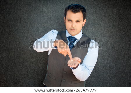 Closeup portrait of mean young man in vest and tie pointing at palm hand, indicating that it is pay day, time to pay up, isolated black gray background