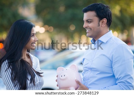 Closeup portrait, smiling happy man in blue shirt and woman holding piggy bank, isolated outdoors background with car and trees. Smart financial investments and advice