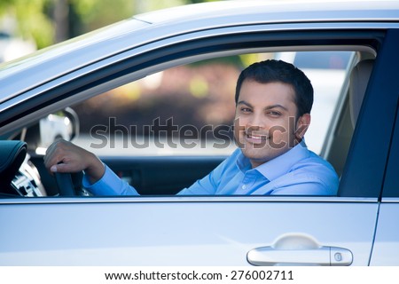 Closeup portrait, young handsome man in his new silver gray car, relaxing, hand on steering wheel, looking out window, isolated on outdoors background with vehicle.