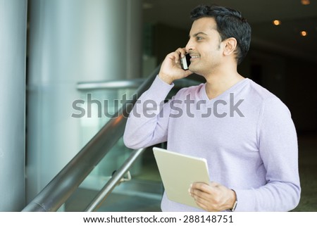 Closeup portrait, side view young business man, happy guy, in purple sweater, using cell phone and tablet, smiling, having pleasant conversation, isolated indoors office. Human emotions, expression