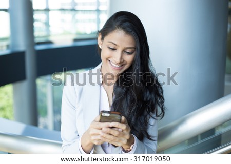 Closeup portrait, young successful happy business woman in light white gray suit, checking her cellphone, isolated on interior indoors office background . Business communication