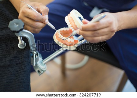 Closeup portrait, young oral professional student practicing dental procedures on plastic teeth, wax typodont mounted on table. Drilling cavity preparations and filling with restorative materials
