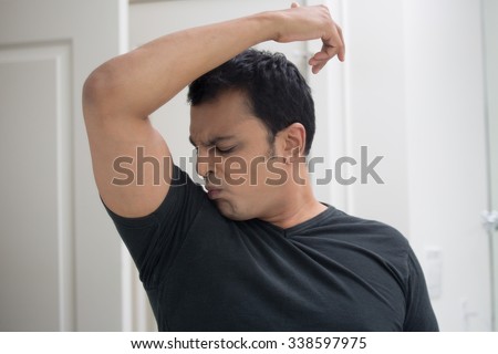 Closeup portrait, grumpy sweaty young man in black t-shirt, sniffing himself, very foul situation, isolated mirror reflection. Negative human emotions, facial expressions, feelings