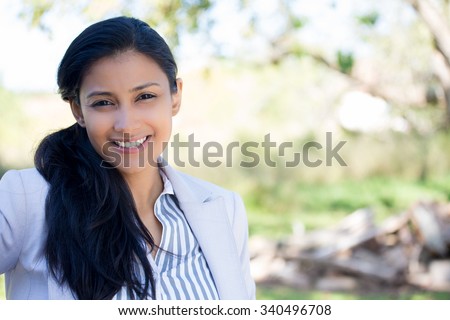 Closeup portrait of confident smiling happy pretty young woman in gray suit, isolated background of blurred trees. Positive human emotion facial expression feelings, attitude, perception