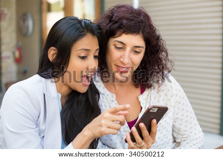 Closeup portrait two surprised girls looking at cell phone discussing latest gossip news, shopping, shocked at what they see, isolated outdoors background