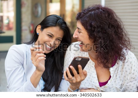 Closeup portrait two surprised girls looking at cell phone, discussing latest gossip news, sharing intimate moments, shopping, laughing at what they see, isolated outdoors background