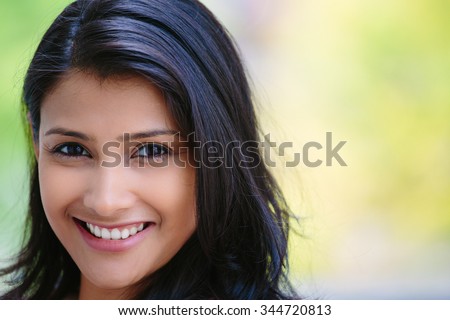 Closeup headshot portrait of confident smiling happy pretty young woman, isolated background of blurred trees. Positive human emotion facial expression feelings, attitude, perception