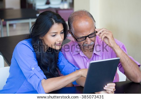 Closeup portrait, sitting young woman showing elderly with black glasses to use portable device,scrutinizing data with great concern, isolated indoors background
