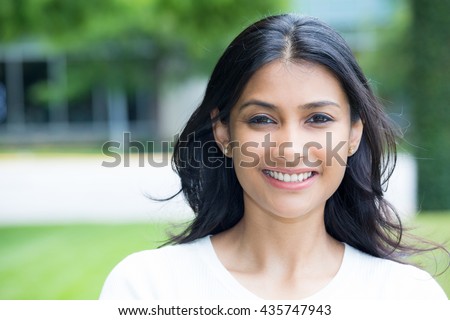 Closeup portrait of confident smiling happy pretty young woman in white shirt, isolated background of blurred trees. Positive human emotion facial expression feelings, attitude, perception