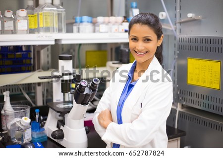 Closeup portrait, young smiling scientist in white lab coat standing by microscope. Isolated lab background. Research and development.