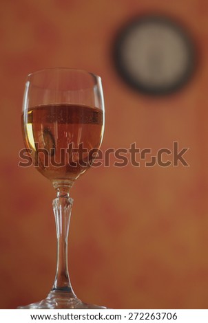 Glass of white wine on a background with a blurred image of a clock.  Alcohol can make you disoriented and can make you losing the sense of time.