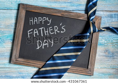 Happy Fathers Day written on chalkboard with blue striped tie on wooden background