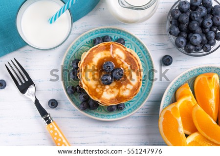 Stack of pancakes with fresh blueberry, honey, milk and orange slices, healthy breakfast concept, top view