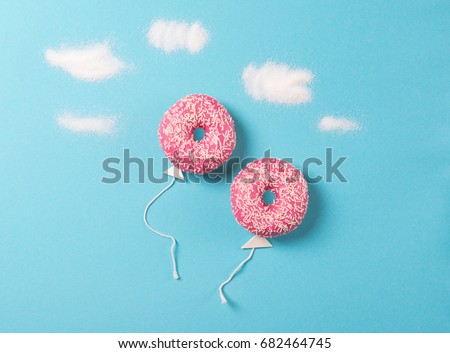 Pink donuts on blue background, creative food minimalism, donut in a shape of balloon in the sky with clouds made of sugar, top view