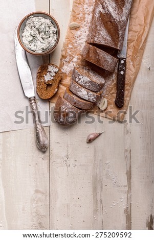 French baguette cut into pieces, garlic, ricotta cottage cheese on a rustic wooden board with knife over light old painted background. Top view