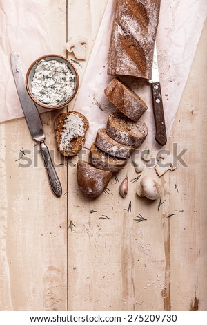 French baguette cut into pieces, garlic, ricotta cottage cheese and mushrooms on a rustic wooden board with knife over light old painted background. Top view