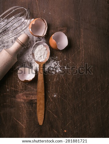 Baking still life of flour spilling out, eggs and rolling pin in natural tone, moody lighting. Tabletop view.