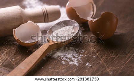 Baking still life of flour spilling out, eggs and rolling pin in natural tone, moody lighting.