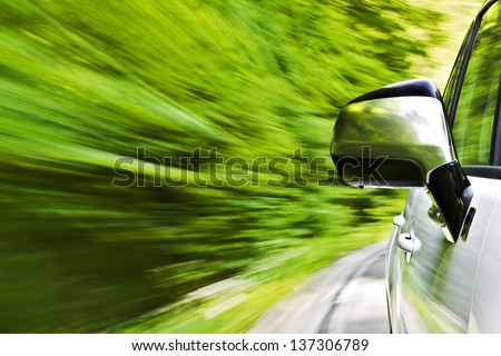 Side view of a luxury car driving fast on a winding road in the woods