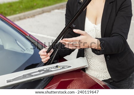 Beautiful girl is changing windscreen wipers on a car