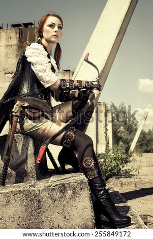 Beautiful redhair woman warrior holding in her hands bow and arrow on the industrial background.