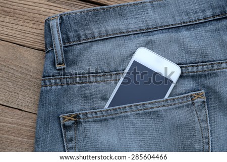Smart phone in the old jeans pocket on wood background