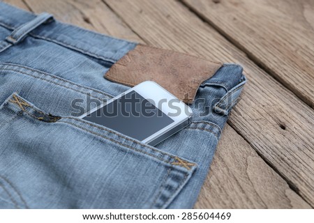 Smart phone in the old jeans pocket on wood background