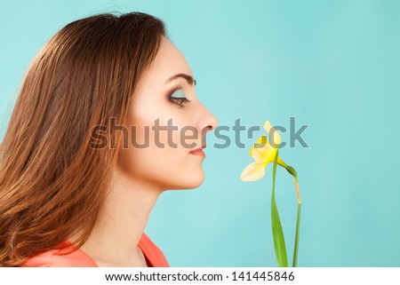 Beautiful woman with makeup smelling narcissus on blue background
