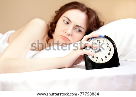 Angry woman lying a bed and holding an alarm (focus on alarm)