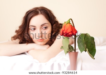 Upset woman in bed looking on the wither  rose (focus on rose)