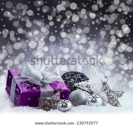 Purple Christmas package , gift of a silver ribbon. Jingle bells , silver christmas balls and christmas stars put on snow. Abstract multicolored blurred background space.