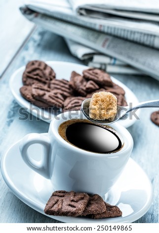 Cup of coffee spoon with cane sugar, chocolate biscuits and the background newspaper. Coffee break.