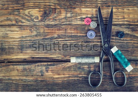 Scissors, bobbins with thread and needles. Old sewing tools on the old wooden background. Vintage Background