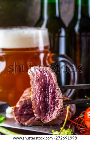 Beef steak.Beef steak with vegetable decoration. In the background cup of beer and bottle full of yeast beer