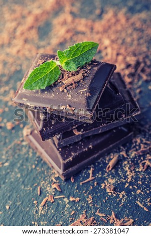 Chocolate. Black chocolate. A few cubes of black chocolate with mint leaves. Chocolate slabs spilled from grated chockolate powder.
