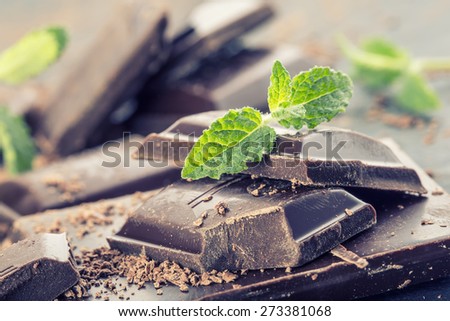 Chocolate. Black chocolate. A few cubes of black chocolate with mint leaves. Chocolate slabs spilled from grated chockolate powder.