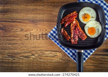 Ham and Egg. Bacon and Egg. Salted egg and sprinkled with black pepper. English breakfast. Grilled bacon, two eggs in a Teflon pan-checked on blue towel on wooden table