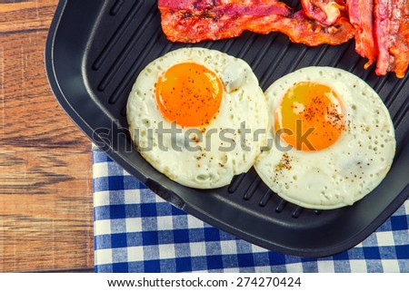 Ham and Egg. Bacon and Egg. Salted egg and sprinkled with black pepper. English breakfast. Grilled bacon, two eggs in a Teflon pan-checked on blue towel on wooden table