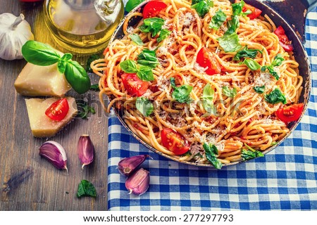 Spaghetti. Italian and Mediterranean cuisine. Spaghetti bolognese with cherry tomato and basil. Spaghetti with tomato sauce on blue checkered tablecloth and rustic wooden table