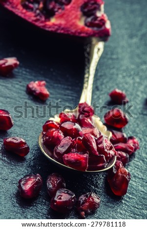Pieces and grains of ripe pomegranate. Pomegranate seeds. Part of pomegranate fruit on granite board and antique spoon. Mediterranean fruit.