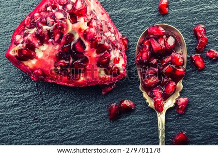Pieces and grains of ripe pomegranate. Pomegranate seeds. Part of pomegranate fruit on granite board and antique spoon. Mediterranean fruit.