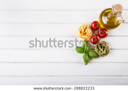 Italian and Mediterranean food ingredients on white wooden background.Cherry tomatoes pasta, basil leaves and carafe with olive oil