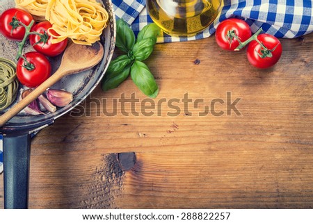 Italian and Mediterranean food ingredients on wooden background.Cherry tomatoes pasta, basil leaves and carafe with olive oil. Wooden and old  kitchen utensils