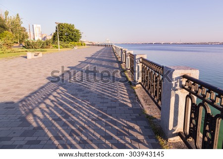 Promenade with paving stone and wrought iron railing in  Dnipropetrovsk city, Ukraine. Summer sunny day - river Dniepr. Road bridge on background.