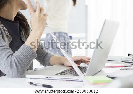 Answer the phone woman while operating a laptop