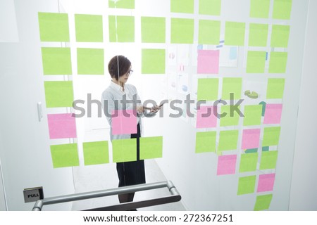 Thinking designer looking at sticky notes on window in creative office