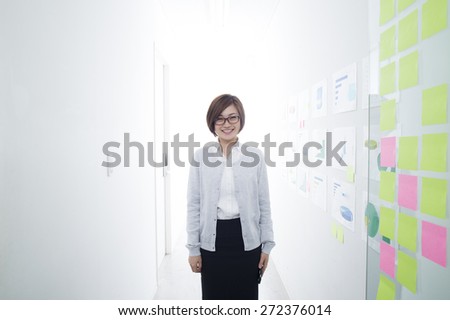 Portrait of smiling businesswoman standing by glass wall with sticky notes in office